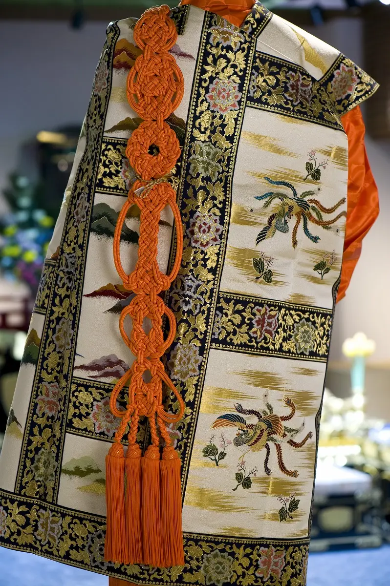 七條袈裟の意匠。金襴地に草花と蝶の刺繍、朱の修多羅が下がる